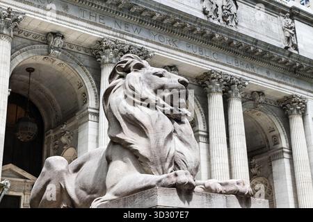 Abgewinkelter Blick auf die Löwenstatue, die den Vordereingang der New Yorker Public Library flankiert, mit defokussierter Fassade im Hintergrund. Stockfoto