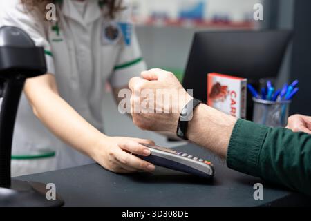 Nahaufnahme eines Seniorenmannes zahlt mit Smart Watch am POS in einer Apotheke, kauft Medikamente und Selbstpflegeartikel in einer modernen High-Tech-Umgebung im Gesundheitswesen. Apotheke. Stockfoto