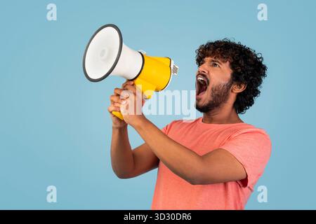 Junger bärtiger Indianer, der leidenschaftlich in ein Megaphon auf rosa Hintergrund spricht Stockfoto