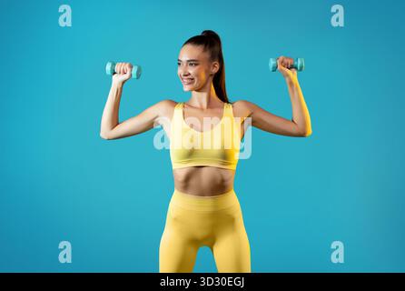 Fitte Frau, die fröhlich mit Kurzhanteln über einem hellen blauen Hintergrund trainiert Stockfoto