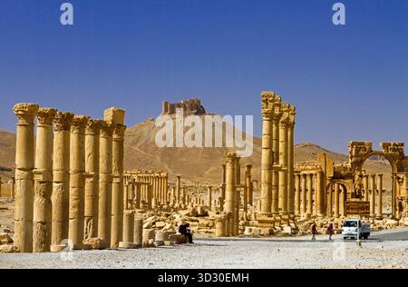 Blick entlang der Großen Kolonnade von Palmyra (Tadmor) in Richtung der Zitadelle auf dem Hügel mit dem Triumphbogen und römischen Säulen in der syrischen Wüste. Stockfoto