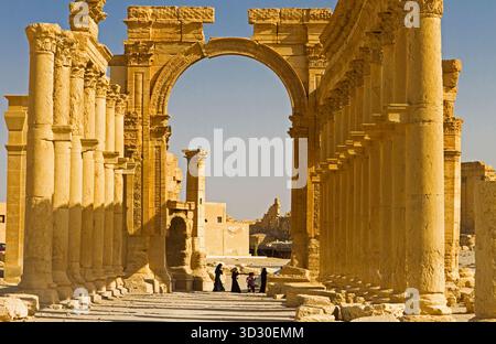 Monumentaler Triumphbogen, eingerahmt von korinthischen Kolonnaden in der antiken Oasenstadt Palmyra (Tadmor), Syrien, mit Menschen, die unter den Ruinen spazieren. Stockfoto