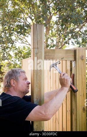 Ein Mann baut eine Holzwand im Garten. Stockfoto