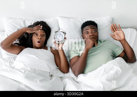 Ein Paar überrascht vom Wecker im Bett, der in einem Morgenmoment überraschend und dringlich war Stockfoto