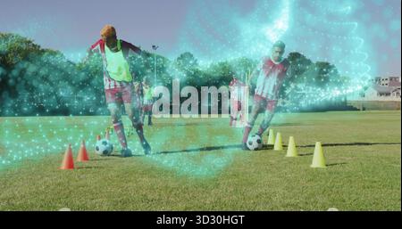 Zwei Spieler in rot-weißen Trikots, die Fußballbälle mit Lätzchen durch die Kegel auf dem Rasenfeld dribbeln Stockfoto