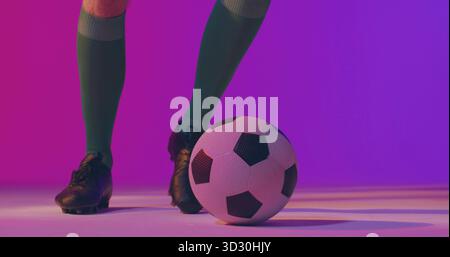 Stehbeine mit grünen Kniestrümpfen und schwarzen Stollen im Studio, mit schwarz-weißem Fußball Stockfoto