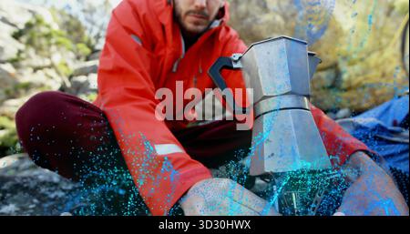 Kniender Wanderer in roter Jacke, der den Campingofen auf felsigem Hügel mit einem Mokakopf aus Metall verstellt Stockfoto