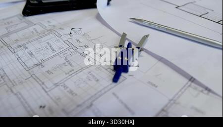 Aufliegender Kompass mit blauem Griff am Schreibtisch mit Grundrissblättern, Blaudruck und mechanischem Stift Stockfoto