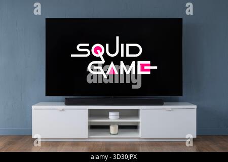 Ein Breitbild-OLED-Fernseher, der die Intro-Szene zur TV-Serie Squid Game in einem modernen Wohnzimmer zeigt. Stockfoto