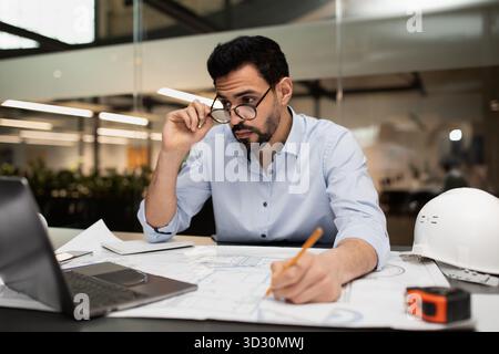 Ingenieur überprüft Blaupausen während der Planung eines neuen Bauprojekts in moderner Büroumgebung Stockfoto