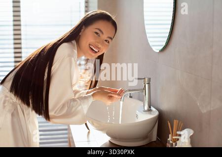 Glückliche langhaarige Frau genießt ihre Morgengesichtswäsche in einem modernen Badezimmer Stockfoto