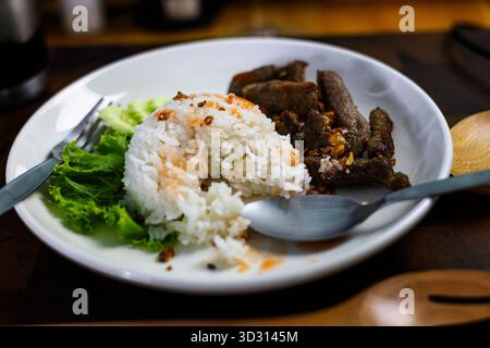 Knoblauch gebratener Schweinefleisch Reis auf Dining Teller, Ein dampfender Teller mit gebratenem Knoblauch Schweinefleisch auf einem Esstisch, knuspriges Schweinefleisch und duftender Knoblauch oben flauschig Stockfoto
