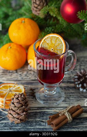 Ein warmes Getränk steht in einem Glas mit Orangenscheiben auf der Oberseite, umgeben von frischen Orangen und Tannenzapfen. Die Szene fängt eine gemütliche, festliche Stimmung mit Witz ein Stockfoto