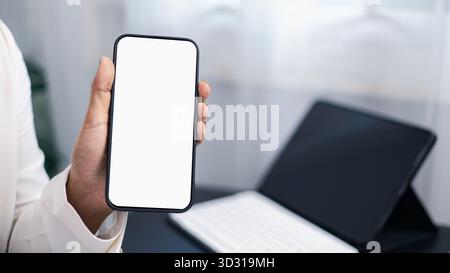 Handheld-Smartphone für Geschäftsleute mit leerem weißen Bildschirm in modernem Büroarbeitsplatz, digitales Technologiekonzept. Stockfoto