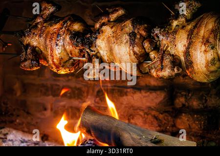 Eine Nahaufnahme ganzer Hühner, die auf einem Rotisserie rösten, spucken über einem offenen Holzfeuer in einem traditionellen Backofen. Stockfoto