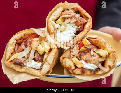 Drei frisch zubereitete griechische Gyros-Wraps gefüllt mit gegrilltem Fleisch, Pommes Frites, Zwiebeln und Tzatziki-Sauce werden auf einem rustikalen Teller mit warmem rotem Background serviert Stockfoto
