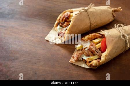 Zwei frisch gewickelte Hühnchen-Gyros mit Pommes, Tomaten und Soße ruhen auf einem rustikalen Holztisch in warmem natürlichem Licht und betonen ihre Textur Stockfoto
