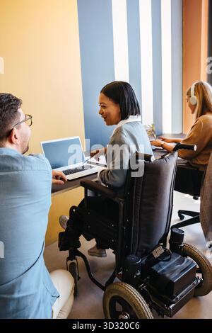 Drei Kollegen, die am Arbeitsplatz diskutieren und sich mit einem Kollegen im Rollstuhl unterhalten. Stockfoto