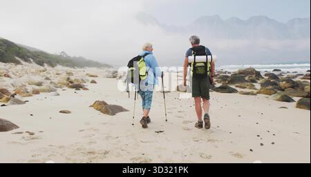 Ein älteres Ehepaar, das die felsige Küste mit Wanderrucksäcken und Trekkingstöcken erkundet Stockfoto