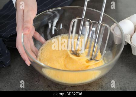Frau, die Eier mit Mixer am grauen Tisch schlägt, Nahaufnahme Stockfoto