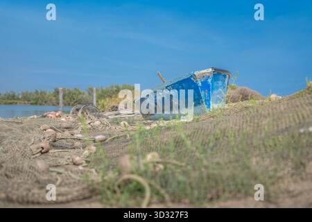 Verwittertes blaues Fischerboot, das auf einer Sandbank mit Fischernetzen und Leinen im Vordergrund an Land gezogen wurde Stockfoto