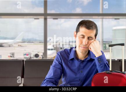 Müder Mann, der in der Flughafenlounge schläft und neben dem Koffer auf seinen Flug wartet Stockfoto
