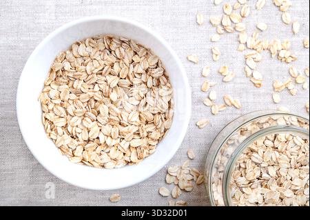 Haferflocken, dickgerollte Haferflocken und altmodische Haferflocken, in einer weißen Schüssel, auf Leinen. Geschälte und gedämpfte Hafergrieß, unter schweren Rollen zu Flocken gerollt. Stockfoto