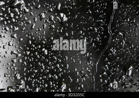 Moody, dramatische Nahaufnahme von Wassertropfen auf dunklem, nassem Hintergrund. Die abstrakte Textur von Kondensation und Regen auf dem Fenster erzeugt düstere, reflektierende sur Stockfoto