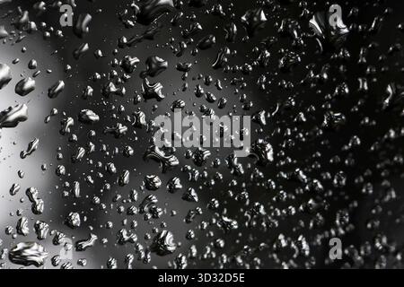 Moody abstrakter Hintergrund von Wassertropfen auf nasser schwarzer Oberfläche. Die flüssige Textur des Regens erzeugt ein ruhiges und reflektierendes Muster voller Feuchtigkeit und Kondenzen Stockfoto