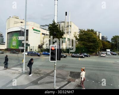 Manchester, Vereinigtes Königreich - 29. September 2025: Menschen überqueren eine geschäftige Manchester Street vor einem Heineken-Gebäude und einer industriellen Kulisse. Stockfoto