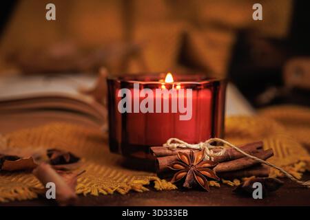 Kerze in herbstlicher Atmosphäre mit Buch und Gewürzen Stockfoto