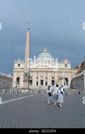 Nonnen spazieren an einem dunklen, bewölkten Tag über den Petersplatz und den Petersdom Stockfoto