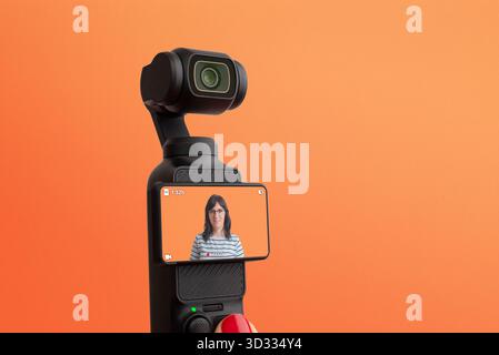Kompakte Handkamera, die Frauen auf orangefarbenem Hintergrund aufzeichnet, Konzept der Vlogging, moderne Kommunikation, Kreativität und digitales Storytelling Stockfoto