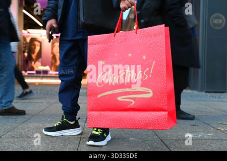 Berlin, Deutschland. November 2025. Ein Mann steht auf einer Einkaufsstraße am Kurfürstendamm in Berlin mit einer Weihnachtstasche mit dem Slogan „Frohe Weihnachten“. Quelle: ELISA Schu/dpa/Alamy Live News Stockfoto
