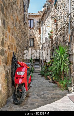 Italien - Bolsena - historische Gasse - schmale Steinpassage mit rotem Roller, Topfpflanzen und rustikalen Fassaden im mittelalterlichen Viertel Stockfoto