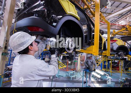 Männer bei der Arbeit. Junger Mann mit Schutzkleidung, der mit Werkzeugen und Maschinen in einer Autofabrik arbeitet Stockfoto
