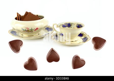 Ein bezauberndes Stillleben mit antikem Goldrand, einem Gericht mit Waffelkeksen und verstreuten herzförmigen Pralinen. Stockfoto