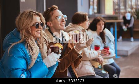 Gruppe junger Freunde, die im Freien lachen und heiße Getränke trinken Stockfoto