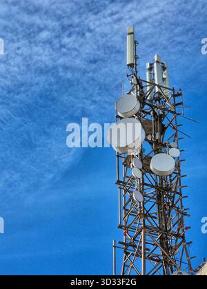 Ein großer Kommunikationsturm (Kommunikationsturm) mit zahlreichen Antennen und Satellitenschüsseln, fotografiert vor einem hellblauen Himmel. Stockfoto