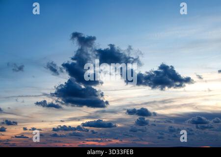 Tiefe Blau- und Orangetöne erfüllen den Himmel, während verstreute Wolken während eines dramatischen Abendsonnenverkehrs über dem Horizont schweben Stockfoto