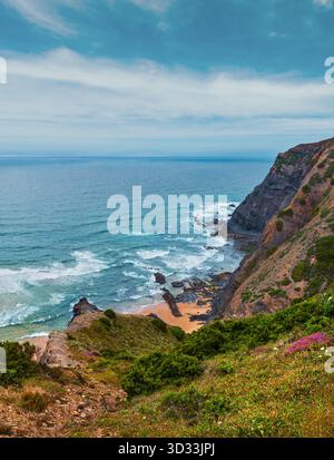 Sandstrand mit felsigen Bergrücken trübes Wetter Aussicht auf Sommer Atlantic an der felsigen Küste (Costa Vicentina, Algarve, Portugal). Und Ocean Surf Wellen. Stockfoto
