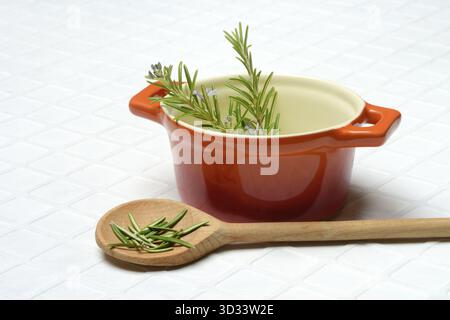 Rosmarin, Rosmarinzweig im Kochtopf und Rosmarinblätter im Kochlöffel Stockfoto