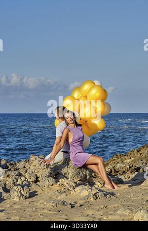 Ruhiges Paar mit gelben Ballons am Ufer des Meeres während entspannender Feiertage, bereit für die Ballonfreigabe von memori Stockfoto