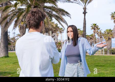 Paare streiten sich draußen im Park mit Palmen während des Konflikts an sonnigen Tagen. Stockfoto