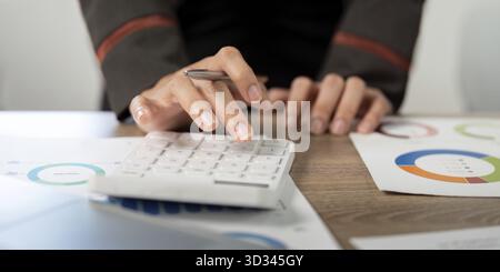 Ein Geschäftsmann, der einen Taschenrechner verwendet, während er Finanzdaten und Diagramme analysiert und dabei Präzision und analytische Fähigkeiten betont Stockfoto