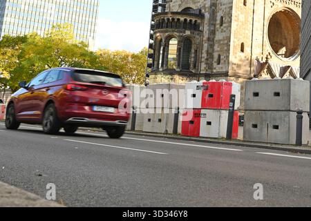 Berlin, Deutschland. November 2025. Ein Auto fährt an gestapelten Betonbarrieren vor der Kaiser-Wilhelm-Gedächtniskirche am Breitscheidplatz in Berlin vorbei. Dort wurden bereits vor der Eröffnung des Weihnachtsmarktes Sicherheitsbarrieren errichtet. Die Barrieren sollen den Weihnachtsmarkt vor möglichen Fahrzeugangriffen während der Adventszeit schützen. Quelle: ELISA Schu/dpa/Alamy Live News Stockfoto