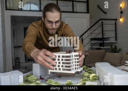Konzentrierter Mann Architekt in Gläsern arbeitet im Büro mit der Schaffung eines neuen Wohnkomplexes, entwirft Layout der Gebäude Stockfoto