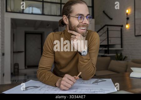 Ein lächelnder junger Architekt, der an Bauplänen im Büro arbeitet, neue Hausentwürfe erstellt, Planung arbeitet Stockfoto
