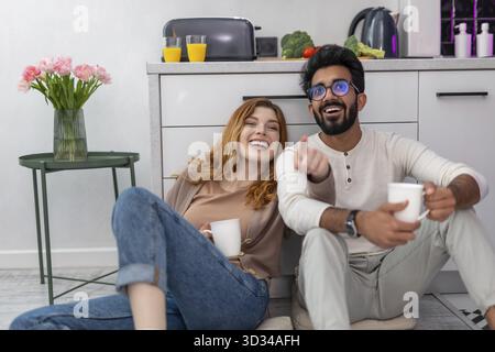 Schöne Frau in Jeans, die auf dem Boden sitzt und mit ihrem Freund spricht, ein Paar genießt Kaffee in der Küche zu Hause Stockfoto