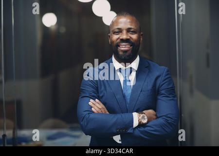 Portrait lächelnder afroamerikanischer Geschäftsmann in blauem Anzug im Büro Stockfoto